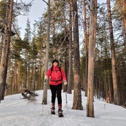 Nainen liukulumikengillä talvisessa metsässä.