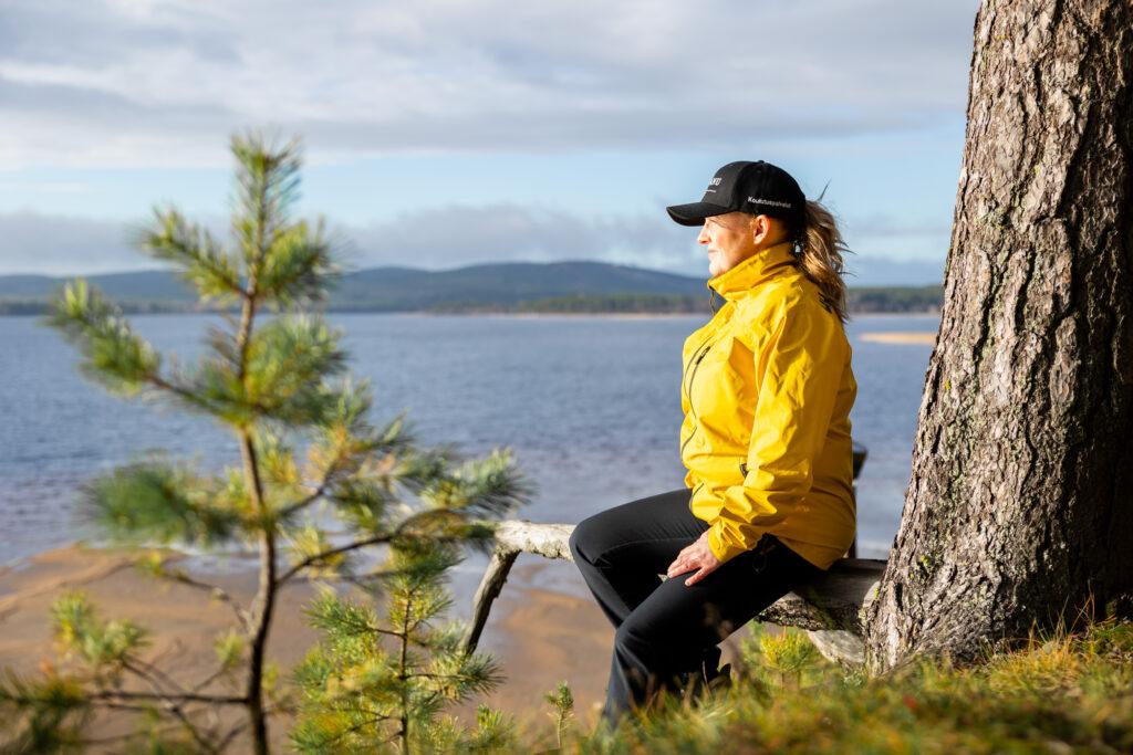 Nainen istuu puunrungolla ja katsoo järvelle